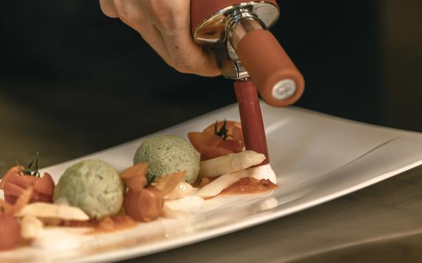 ein koch gibt nussbutterschaum mit dem isi auf einen teller im restaurant feuergott im vulkanlandhotel legenstein in bad gleichenberg
