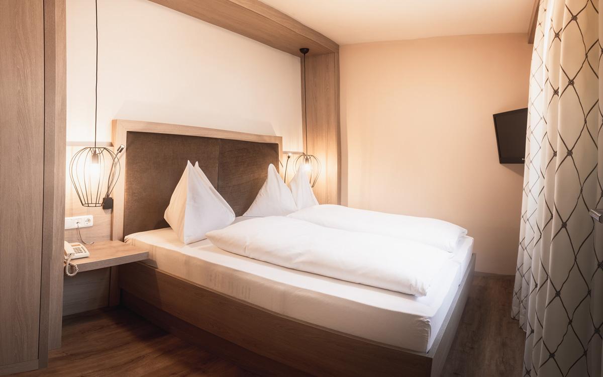 Schlafzimmerübersicht Bett mit weißer Bettwäsche und Nachttisch darüber hängen moderne Leuchten im minimalistischen Stil in der Suite Sulzberg - Preise im Vulkanlandhotel Legenstein in Bad Gleichenberg