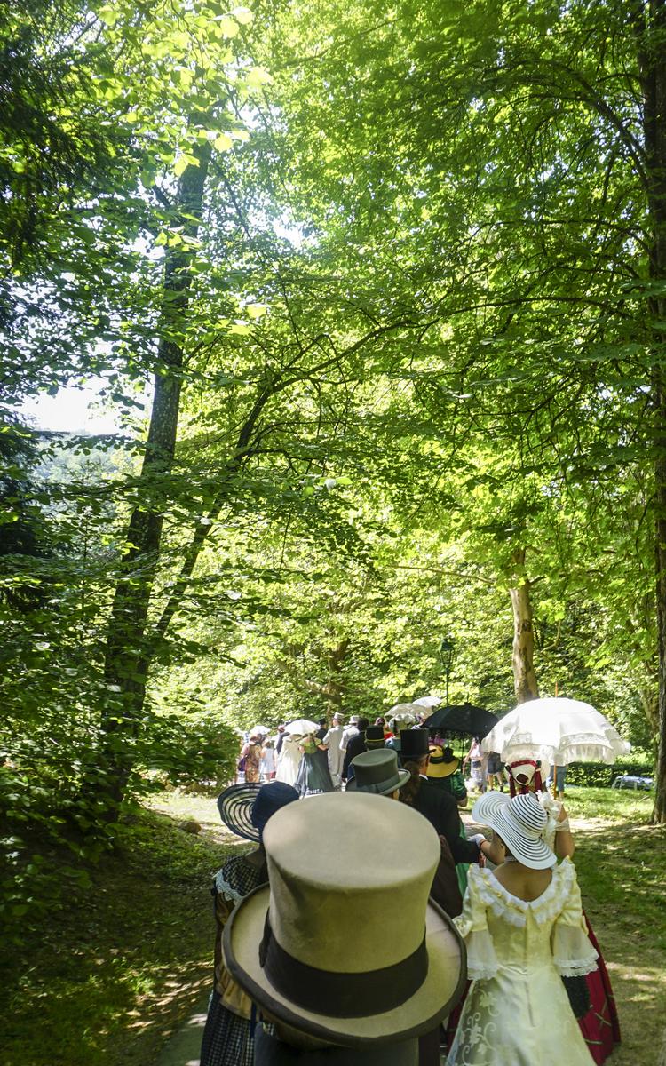 Am Bild sehen Sie Impressionen vom Biedermeierfest in Bad Gleichenberg - Menschen spazieren mit Biedermeier-Kleidern und -Röcken durch den Kurpark - Ausflugsziel vier Jahreszeiten - Vulkanlandhotel Legenstein