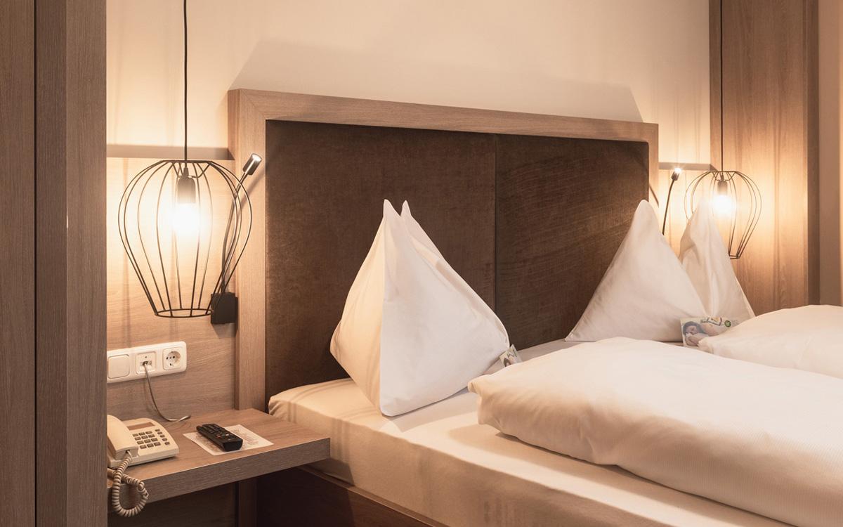 Schlafzimmerdetails Bett mit weißer Bettwäsche und Nachttisch darüber hängen moderne Leuchten im minimalistischen Stil in der Suite Sulzberg - Preise im Vulkanlandhotel Legenstein in Bad Gleichenberg