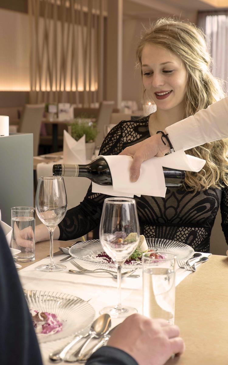 Frau sitzt mit Partner am Tisch im Restaurant Feuergott und lässt sich ein Glas Wein einschenken - Kulinarik, Wandern und Wein im Thermen- und Vulkanland Steiermark - Preise im Vulkanlandhotel Legenstein