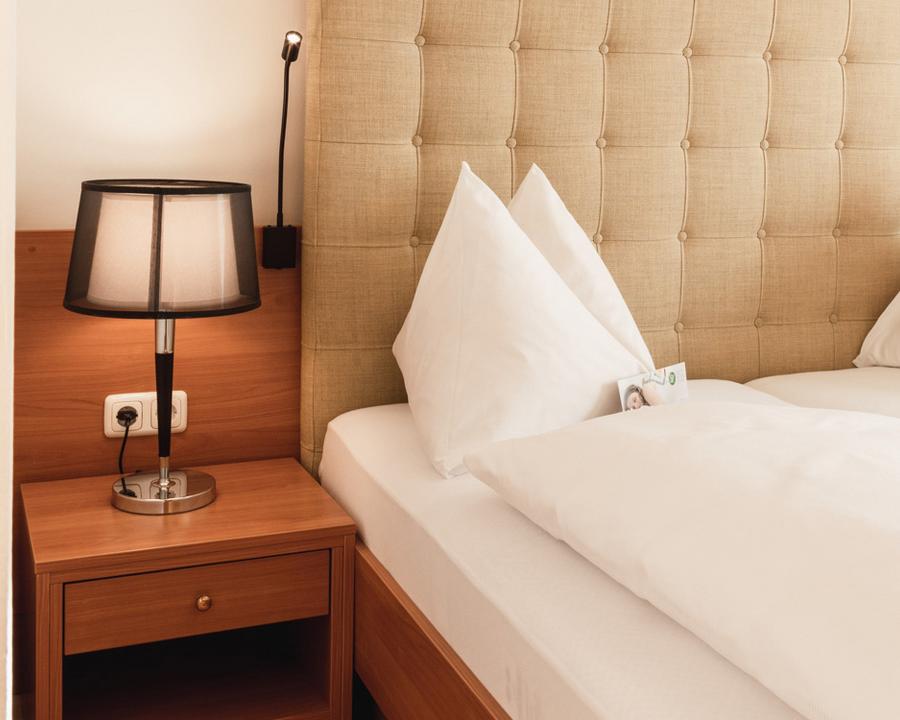 Bett mit Nachttisch und Lampe im Doppelzimmer Cirkonia - Preise im Vulkanlandhotel Legenstein in Bad Gleichenberg