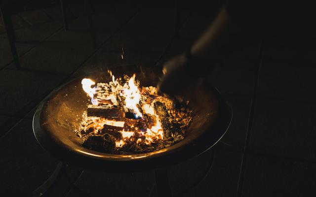 Eine Feuerschale mit Holzscheiteln und Feuer und eine Person wirft einen Zettel hinein - Feuerritual am Silvesterabend im Vulkanlandhotel Legenstein in Bad Gleichenberg