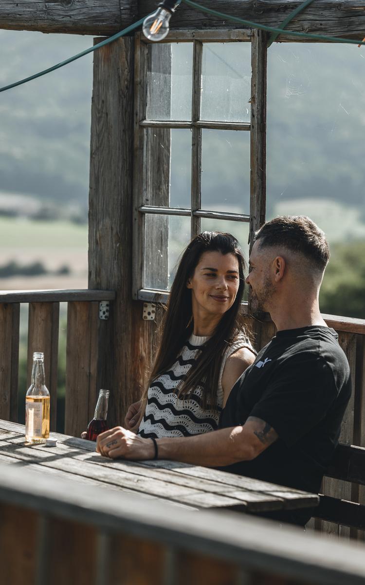 ein pärchen sitzt am parapluieberg im weingarten und genießt ein getränk in der holzhütte in der nähe des vulkanlandhotel legenstein in bad gleichenberg