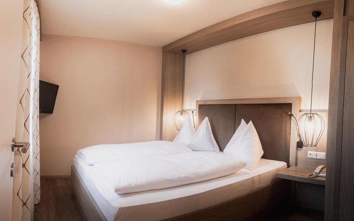 Schlafzimmer aus Eichenholz mit modernen minimalistischen schwarzen Lampen und Doppelbett mit weißer Bettwäsche in der Suite Parapluie - Preise im Vulkanlandhotel Legenstein in Bad Gleichenberg