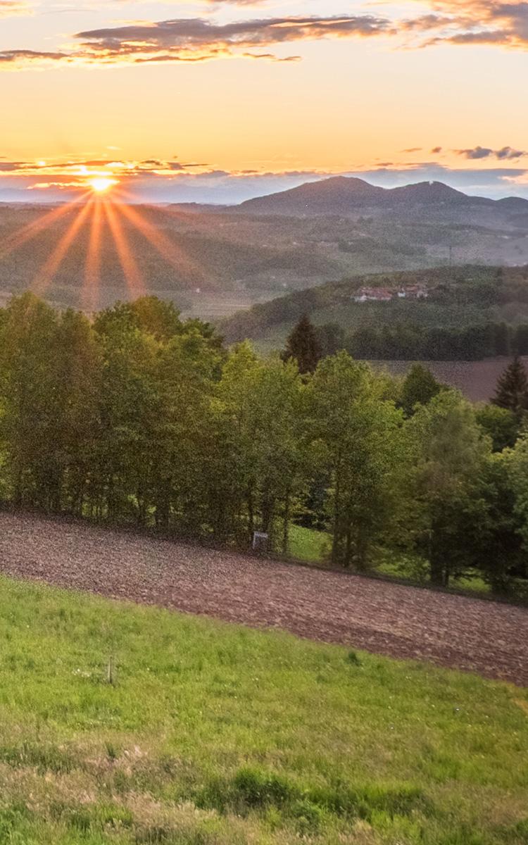 die sonne geht zwischen gleichenberger kogel und stradner kogel unter und symbolisiert den wanderweg 3-kogel-weg im thermen- und vulkanland steiermark verbunden mit urlaub im vulkanlandhotel legenstein in bad gleichenberg