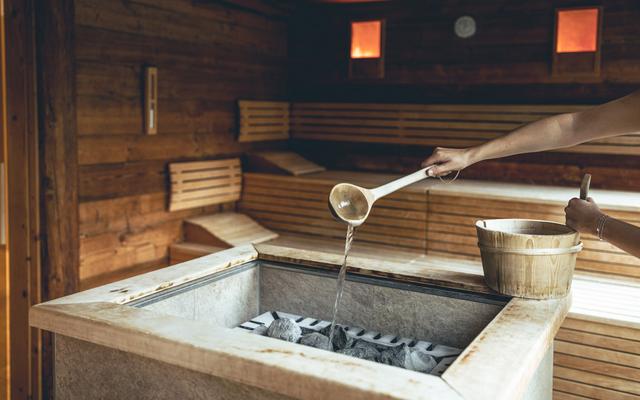 am bild sieht man eine hand, die den saunaschöpfer hält und einen aufguss in der finnischen sauna im vulkanlandhotel legenstein vorbereitet