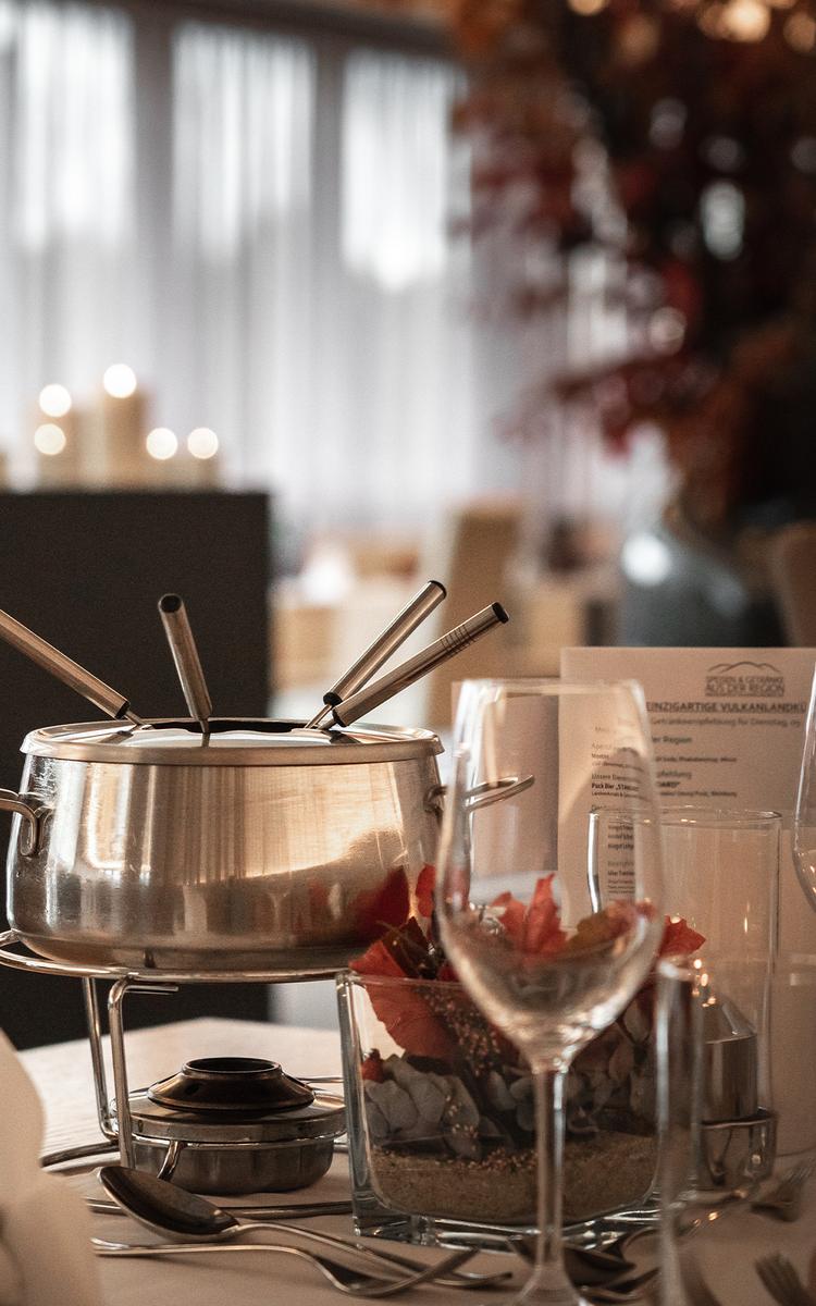 Dampfendes Suppenfondue im Restaurant Feuergott mit frischen Zutaten und Saucen auf dem gedeckten Tisch im Vulkanlandhotel Legenstein.