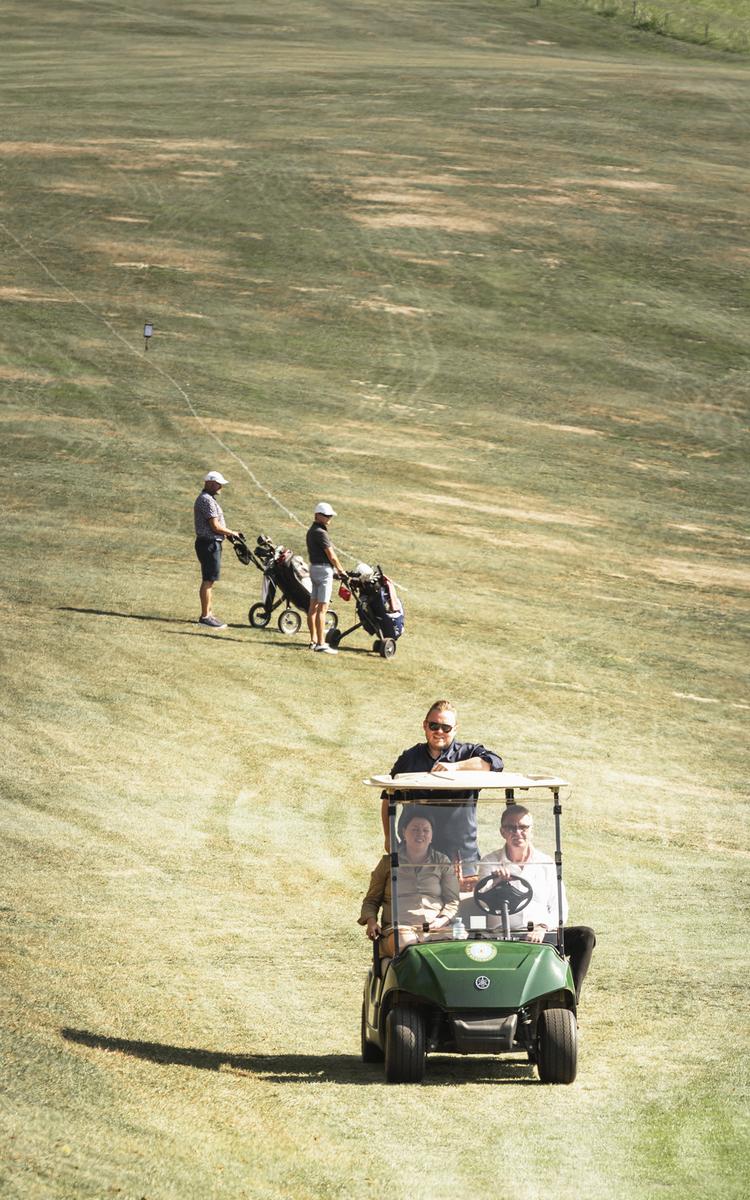 Herbsturlaub in Bad Gleichenberg - zwei männer und eine frau fahren mit dem Golfcar über den Golfplatz und weitere personen spielen golf